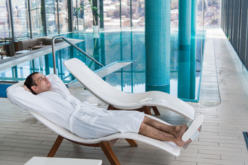 Man in bathrobe relaxing near indoor swimming pool in luxury spa