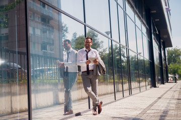 Picture of a confidence successful businessman leaned on building wall, holding his digital tablet and smiling.