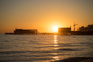 Fototapeta premium Bright orange sunset over the sea pier of the city.
