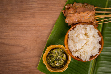 grilled pork or moo ping in Thai with sticky rice and Nam Prik Num (Northern Thai Green Chilli Dip) local street food on banana green leaf