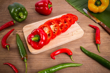 Slices of red bell pepper on wood background with wooden board