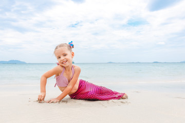 Little beautiful girl dressed in swimsuit as a mermaid sits on the seashore