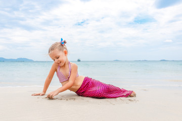 Little beautiful girl dressed in swimsuit as a mermaid sits on the seashore
