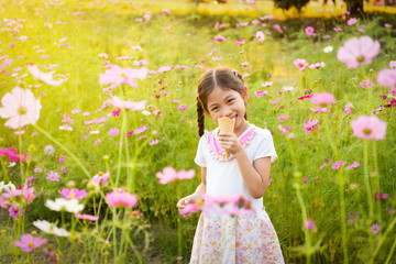 Cute little girl eating ice cream  in the field of pink flowers at sunlight