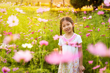 Cute little girl eating ice cream  in the field of pink flowers at sunlight