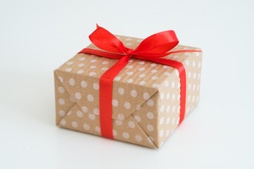 new year present in gift box wrapped in craft dotted paper and tied with a red ribbon bow. package on white background with copyspace.