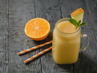 Freshly made melon, orange and banana smoothies and two cocktail tubes on a wooden table.