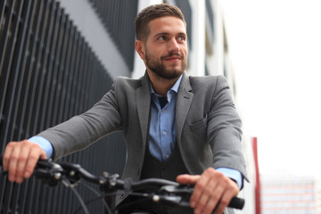 Handsome young businessman riding bicycle outdoors in the city.