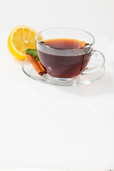 A glass cup with black tea on a saucer with mint, cinnamon, as well as lemon