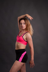 Fototapeta na wymiar Beautiful, athletic, slender woman in a pink T-shirt and black shorts on a dark background
