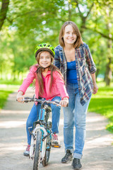 mom teaches her daughter to ride a bicycle in the park