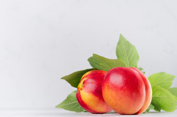 Ripe red nectarines with green leaves closeup on soft white wood board. Sweet summer fruits.