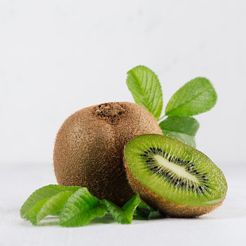 Ripe green kiwi with half cut and juice drop flow down and young leaves on white wood board as fresh summer fruits background, square.