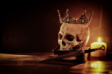 Human skull, old book, sword, crown and burning candle over old wooden table and dark background. - obrazy, fototapety, plakaty