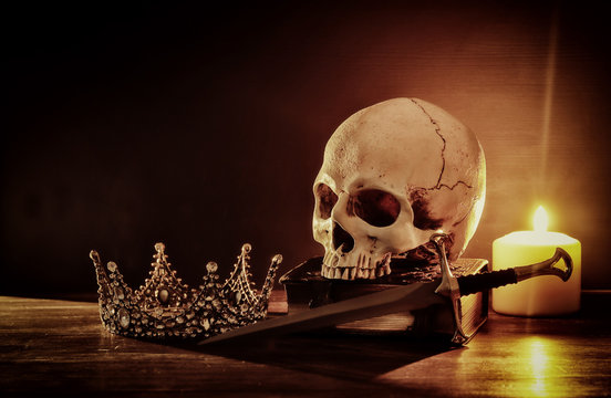 Human skull, old book, sword, crown and burning candle over old wooden table and dark background.