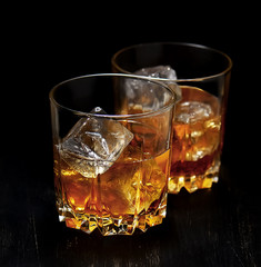 Two glasses with ice and whiskey on wooden background