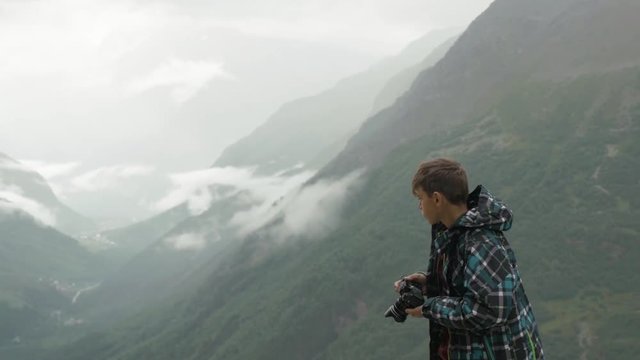 A teenager takes pictures of a mountain landscape.