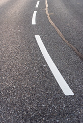 fragment of street with asphalt, in the middle of white belts separating the sides of the roadway, next to them breaks