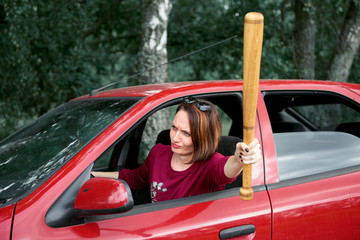young female driver has stress and anger, threatens with a baseball bat, has a red car