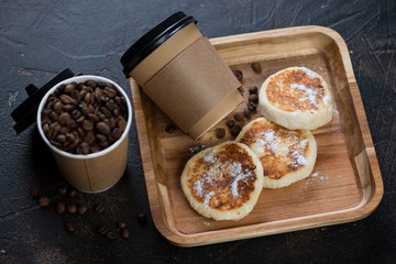 Wooden serving tray with cottage cheese pancakes and takeaway coffee, studio shot, selective focus