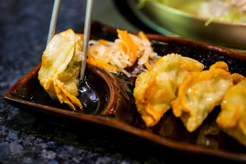 gyoza on chopsticks and souce. Japanese Dumplings with chopsticks. Japanese food, Gyoza on wooden plate with chopsticks and soy sauce.