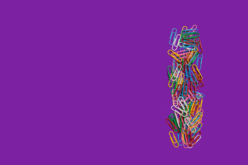 colorful paper clips lying making a line on a purple background. free space for advertising text....