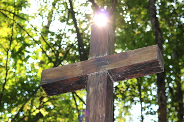 Wooden Christian religious cross on the background of green trees and rays of sunlight at dawn