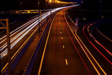 Fototapeta na wymiar Cars light trails on a curved highway at night. Night traffic trails. Motion blur. Night city road with traffic headlight motion. Cityscape. Light up road by vehicle motion blur.