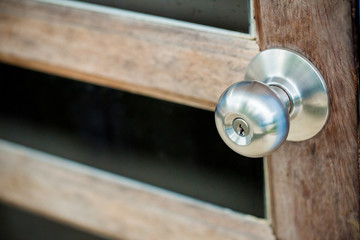 wooden door with grill, stainless door knob or handle on wooden door in beautiful lighting.a handle on a door that is turned to release the latch.