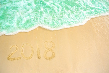 Fototapeta na wymiar Year 2018 written at the sand beach with sea wave water. wave coming to 2018 concept on the sand beach in the morning.Text 2018 on a beach sand. Concept New Year 2018 is coming soon
