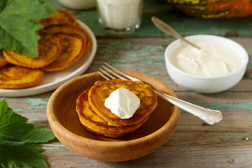 Homemade pumpkin pancakes with sour cream, ripe pumpkin and pumpkin leaves.