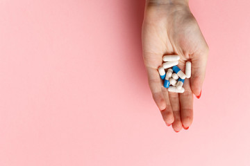 Colorful pills and tablets in the woman hand on pink background. Top view. Flat lay. Copy space. Medicine and health care concept