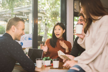 Group of friends chatting and using laptop in cafe at the coffee shop cafe in university talking and laughing together, view through glass.