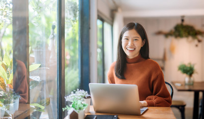 Happy young Asian girl working at a coffee shop with a laptop - Powered by Adobe
