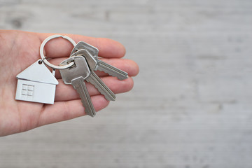 Hand holding and giving key chain with house shaped pendant on blurred natural wood background with...