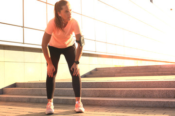 Young fitness attractive sporty girl resting after intensive evening run outdoor at sunset in city.