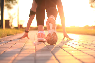 Young fitness attractive sporty girl runner in start position, closeup on shoe, outdoor at sunset or sunrise. - obrazy, fototapety, plakaty