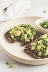 Avocado toast with whole wheat bread, avocado and green onion on white plate.