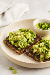 Avocado toast with whole wheat bread, avocado and green onion on white plate.