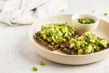 Avocado toast with whole wheat bread, avocado and green onion on white plate.