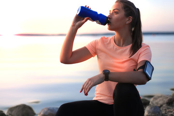 Young attractive sporty fitness woman drinking water exercise in beach outdoor portrait, at sunset...