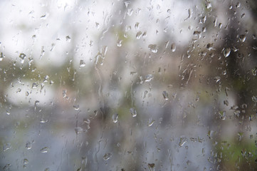 Rain droplets running down on a window, abstract background. Autumn fall season concept. Cloudy boring day indoor