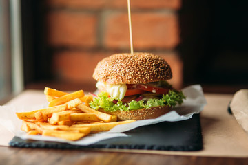 Large tasty burger with French fries in a cafe on a black tray