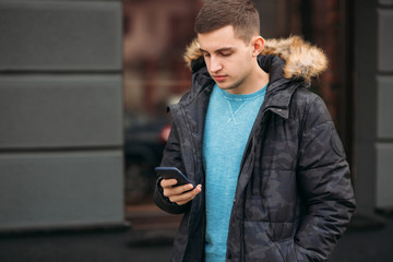 Man in a gray jacket is standing outside and using a phone