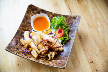 fried squids in wood plate.Steamed squid fried with salty sauce Thai food.Grilled squid and vegetable with spicy seafood sauce on  wood table.