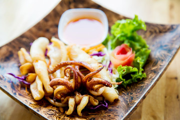 fried squids in wood plate.Steamed squid fried with salty sauce Thai food.Grilled squid and vegetable with spicy seafood sauce on  wood table.
