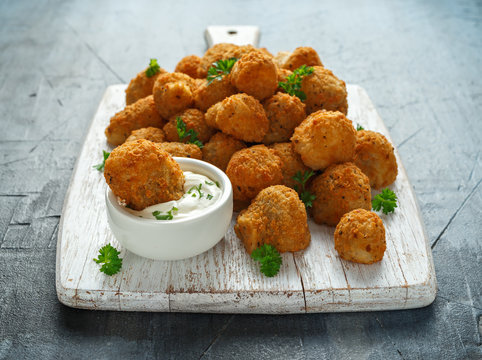 Homemade Breaded Garlic Mushrooms with sour cream and parsley on white wooden board