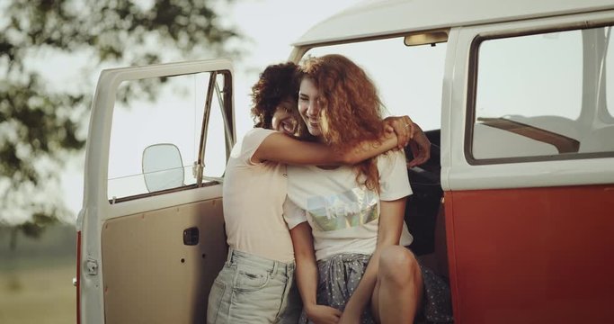Photogenic curly hair girls with perfect white smilie , have a good time together in a bus sitting outside hugging each other.