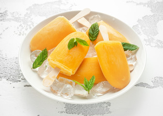 Popsicles, ice lollies on stick with sweet orange juice in white plate with ice
