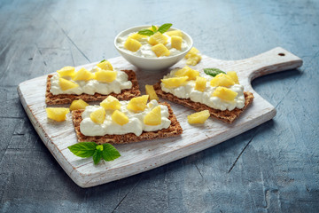 Homemade Crispbread toast with Cottage Cheese and Pineapple on white wooden board.